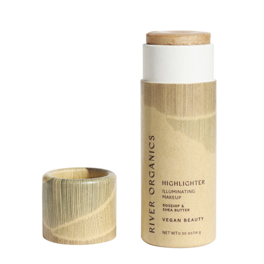 The Illumi Vegan Highlighter Stick - Golden Hue by River Organics, with its cylindrical tube and cap off, reveals the organic illuminator inside. The minimalist eco-friendly packaging in natural tones highlights this clean beauty gem featuring rosehip and shea butter for a warm champagne glow.