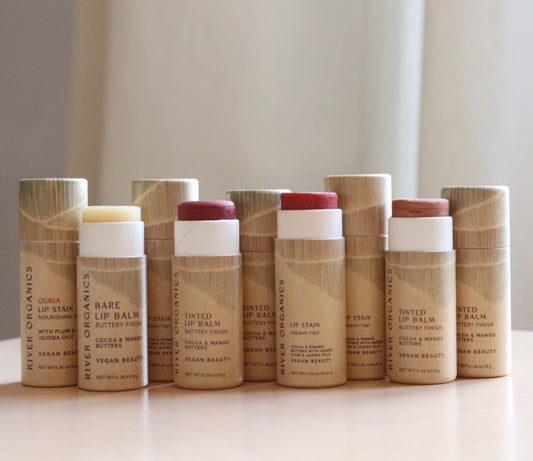 Nine River Organics "Set of 2 Lip Balms or Lip Stains" are arranged in two rows on a neutral surface, each in natural-toned, eco-friendly packaging with minimalistic labels.