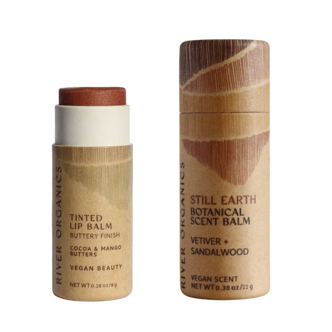 River Organics’ Lip + Scent Balm Bundle includes a Vegan Lip Balm with a buttery finish and a Still Earth Scent Balm (vetiver, sandalwood), both in earthy-toned cylindrical tubes—perfect for your Botanical Ritual.