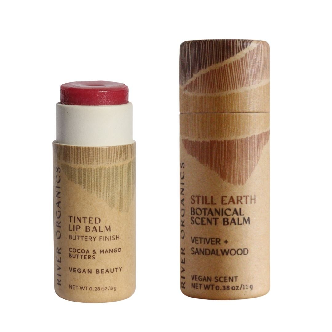 River Organics’ Lip + Scent Balm Bundle includes a vegan cocoa-mango lip balm (red, open tube) and a Still Earth vetiver-sandalwood scent balm (closed tube), both in eco-friendly packaging.