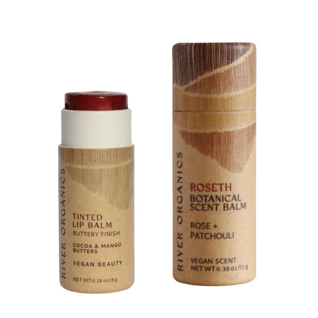 River Organics' Lip + Scent Balm Bundle features two eco-friendly cylindrical tubes: a Vegan Lip Balm with a reddish tint and a Roseth Scent Balm (rose & patchouli), both in brown minimalist packaging.
