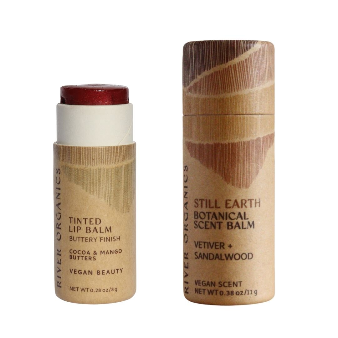 Two cylindrical cardboard tubes of River Organics’ Lip + Scent Balm Bundle, featuring minimalist brown labels—one Lip Balm (partially open with red balm) and one Scent Balm—ideal for your Botanical Ritual.