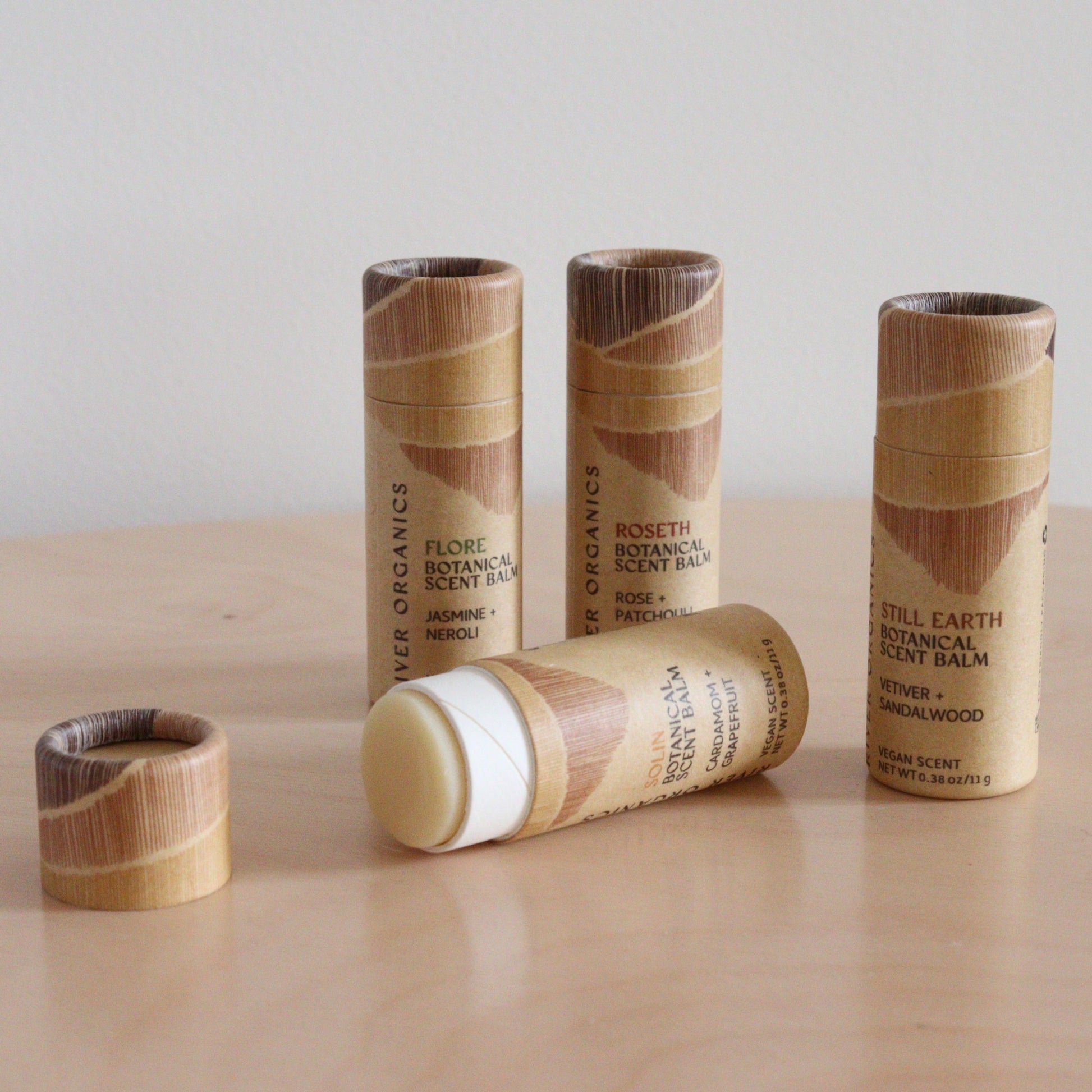 Four River Organics Botanical Scent Balms stand on wood, one open to reveal solid perfume. Each tube features a unique blend of natural scents and essential oils. Available in sets of 2, 3, or 4.