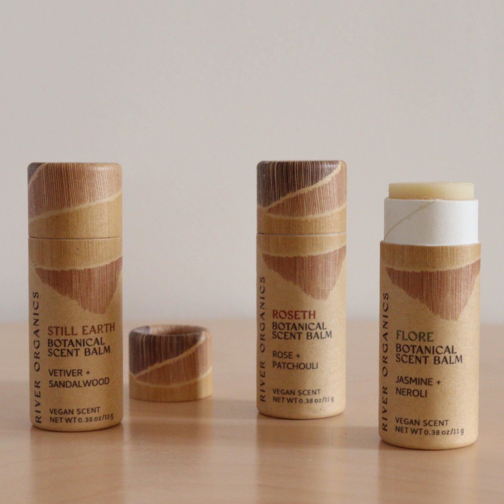 Three River Organics Botanical Scent Balms stand on a light surface: two are closed, labels visible, while one is open to show the balm. This set of 2, 3 or 4 balms features solid perfumes with essential oil blends such as Still Earth and Flore.