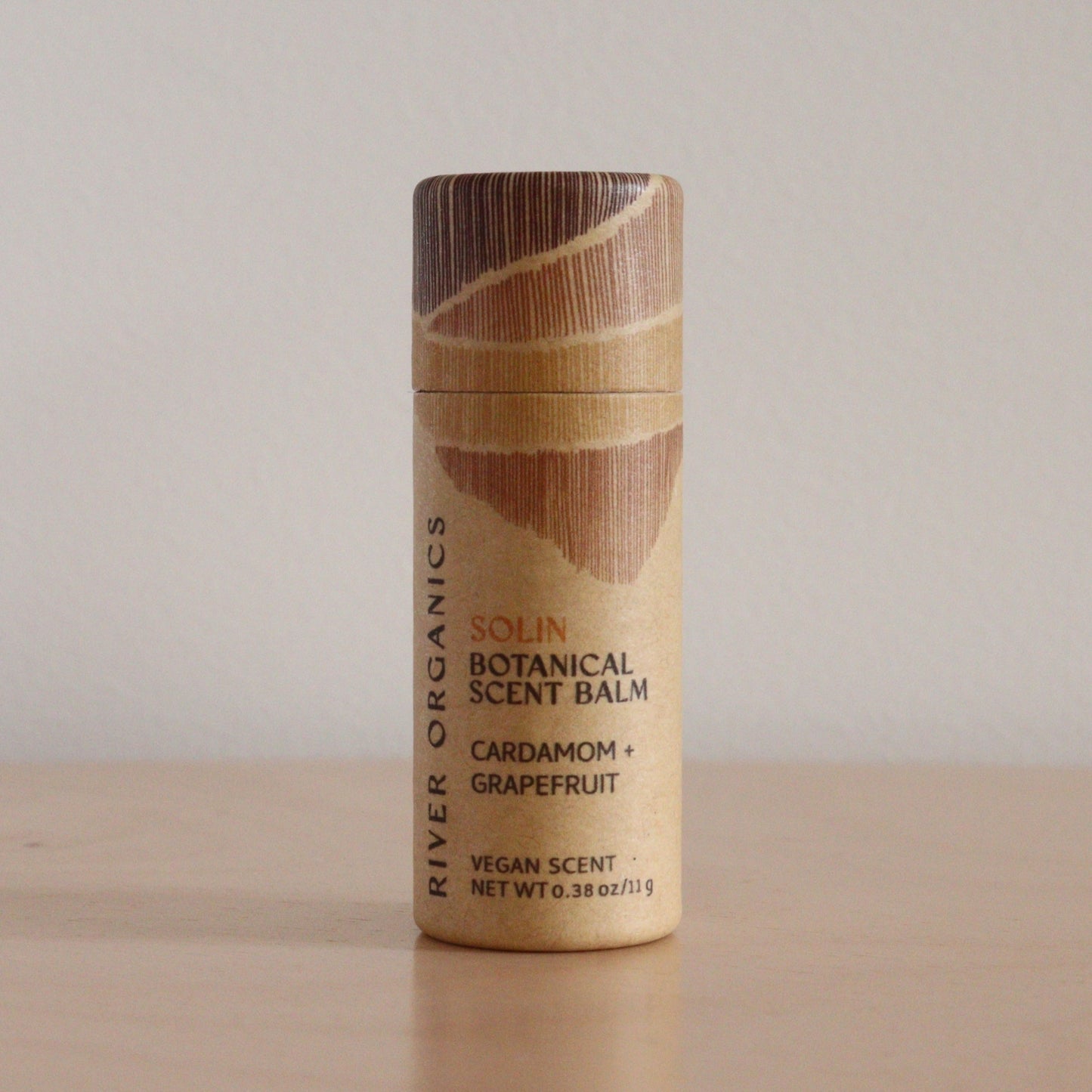 A cylindrical, eco-friendly tube of River Organics Solin: Cardamom + Grapefruit - Botanical Scent Balm stands upright on a light surface against a plain background, emphasizing its natural fragrance and organic ingredients.