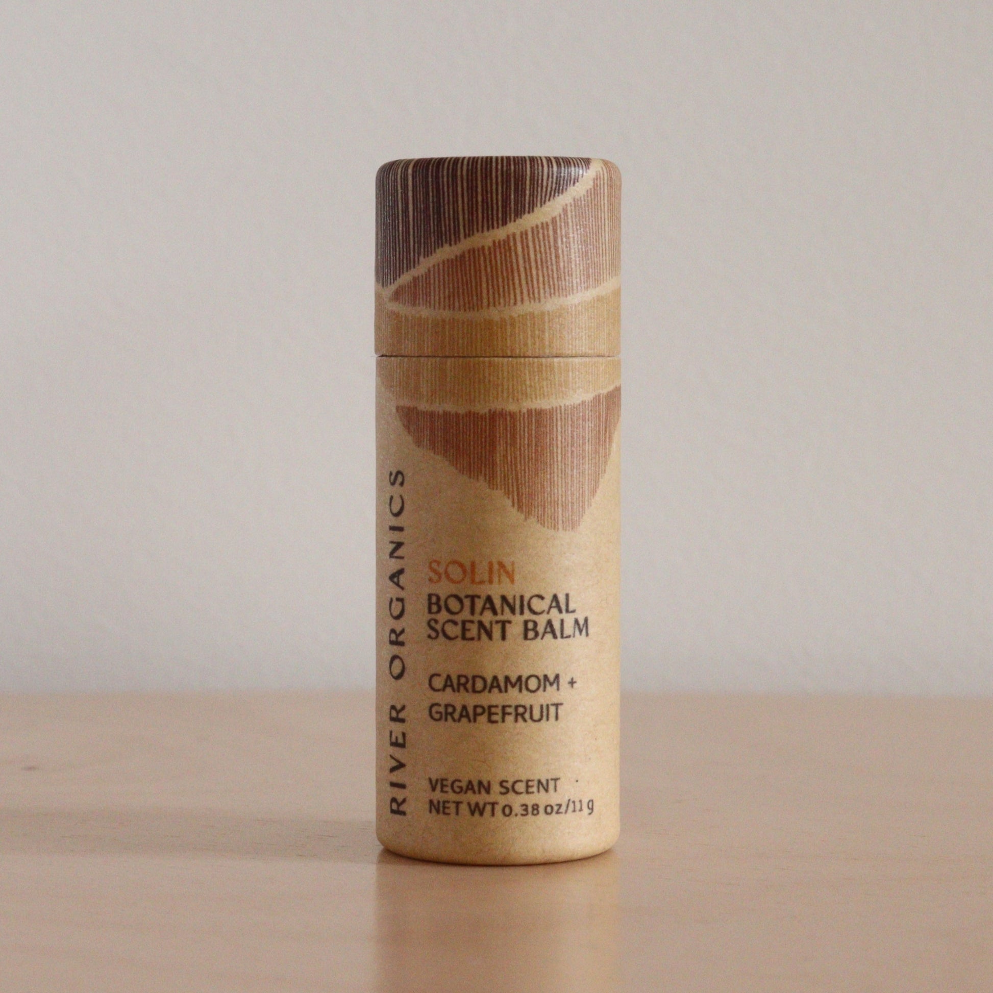 A cylindrical, eco-friendly tube of River Organics Solin: Cardamom + Grapefruit - Botanical Scent Balm stands upright on a light surface against a plain background, emphasizing its natural fragrance and organic ingredients.