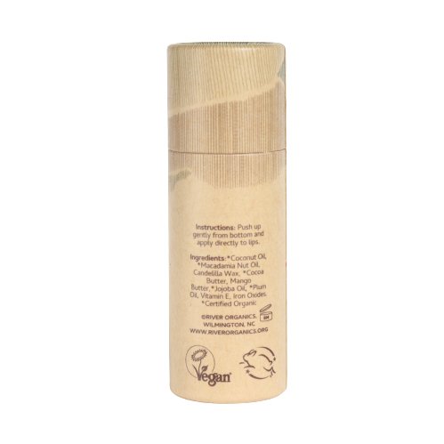 A cylindrical bamboo container of Pomegranate Vegan Lip Stain from River Organics stands upright. The label details instructions to gently push up from the bottom to apply and lists organic ingredients such as coconut oil and cocoa butter. The product, featuring eco-friendly packaging, is certified vegan and offers moisturizing lip care.