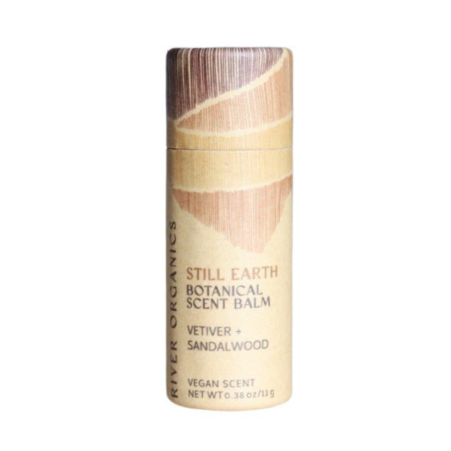 A cylindrical tube of River Organics’ Still Earth: Vetiver + Sandalwood - Botanical Scent Balm features tan packaging with abstract brown designs, reflecting the vegan, botanical scent and rich, natural perfume.