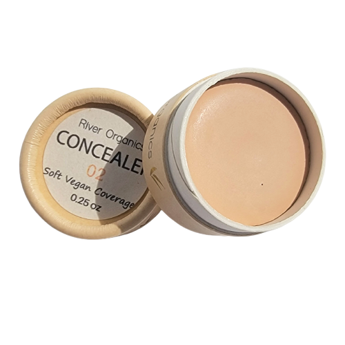 A round container of River Organics Imperfect Natural Hydrating Vegan Concealer, lid off to reveal creamy product. Made with organic plant oils for soft vegan coverage. Label reads "0.25 oz." Shade: 02.