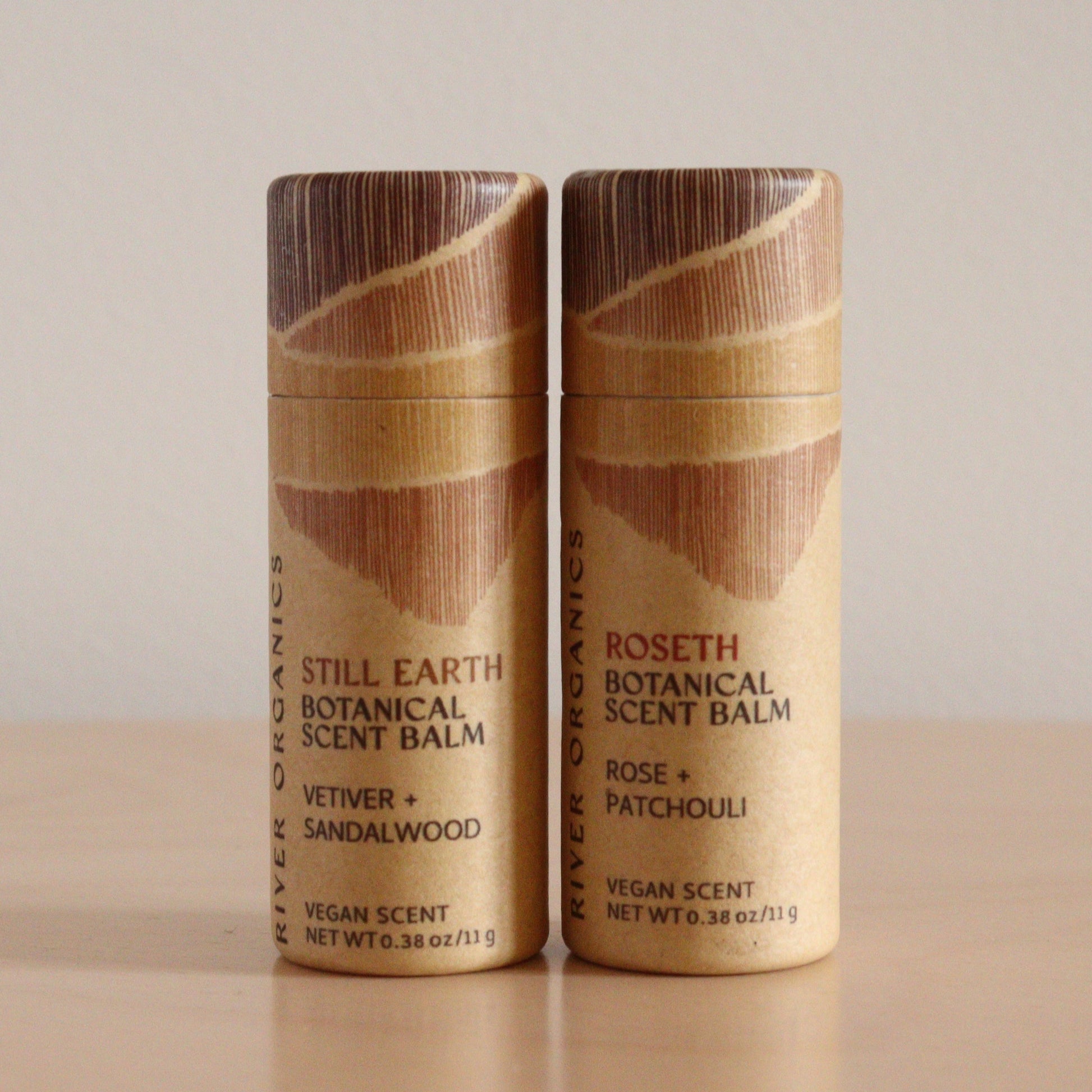 Two cylindrical River Organics Botanical Scent Balm tubes from the Set of 2 are side by side on a light surface, labeled "Still Earth" (left) and "Roseth" (right), each crafted with nourishing plant oils.