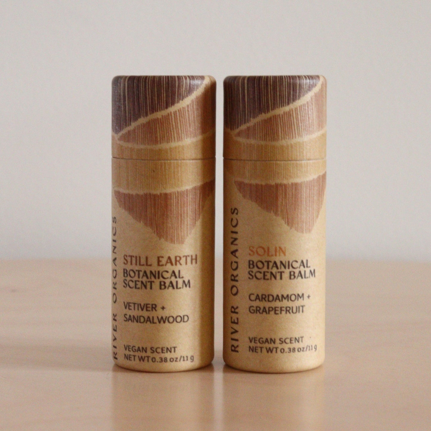 Two River Organics Botanical Scent Balms from the "Set of 2, 3 or 4"—"Still Earth" (Vetiver + Sandalwood) and "Solin" (Cardamom + Grapefruit)—crafted with plant oils, stand side by side on a light wooden surface.