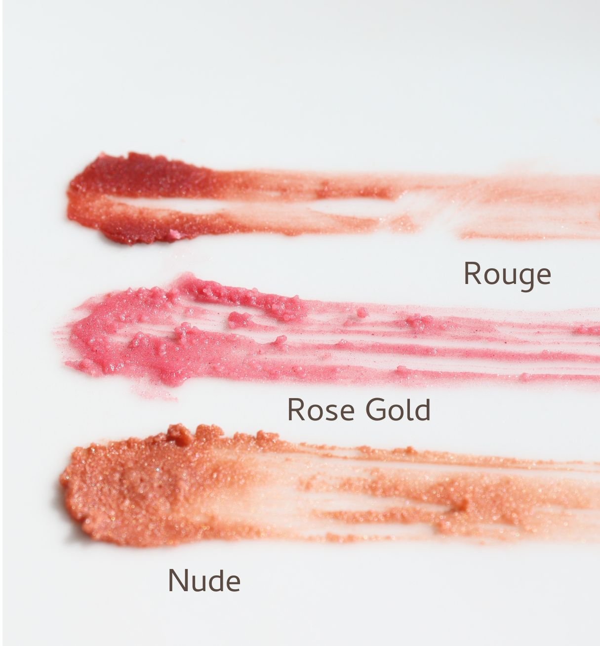 Three swatches of River Organics Tinted Vegan Lip Balms with plant-based ingredients are smeared on a white surface, labeled top to bottom: "Rouge" (red), "Rose Gold" (shimmery pink), and "Nude" (shimmery beige).