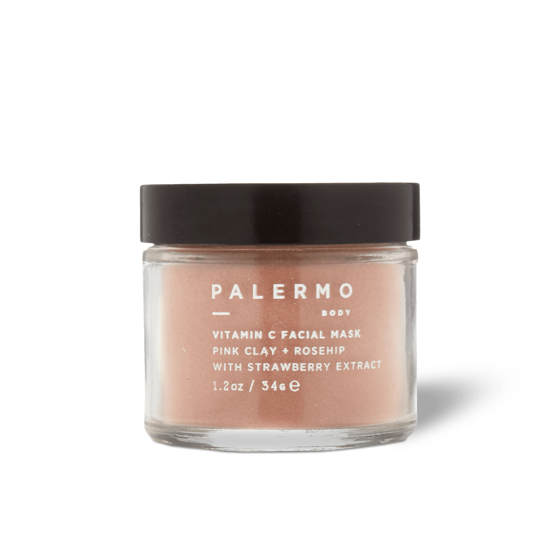 A clear glass jar with a black lid holds Palermo Body's Vitamin C Facial Mask, made with pink clay, rosehip, and strawberry extract for gentle exfoliation. The front label displays white text.
