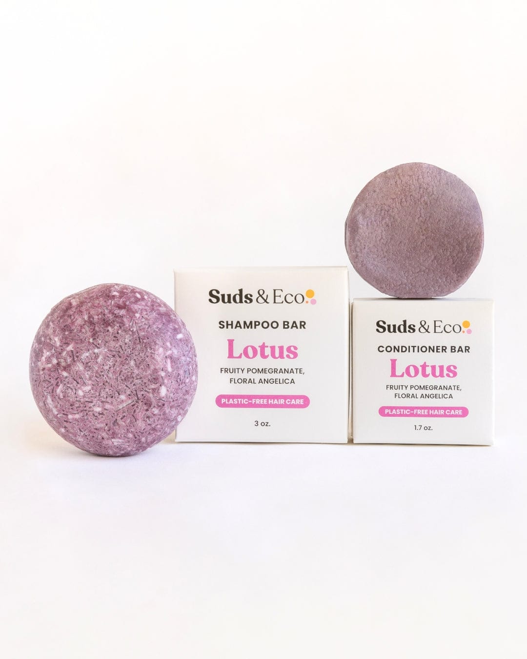 Two round, purple Vegan Shampoo & Conditioner Bar Duo from ZeroWasteStore.com in fruity pomegranate and floral angelica scents with labeled boxes are displayed on a white background—ideal for a zero waste hair care routine.