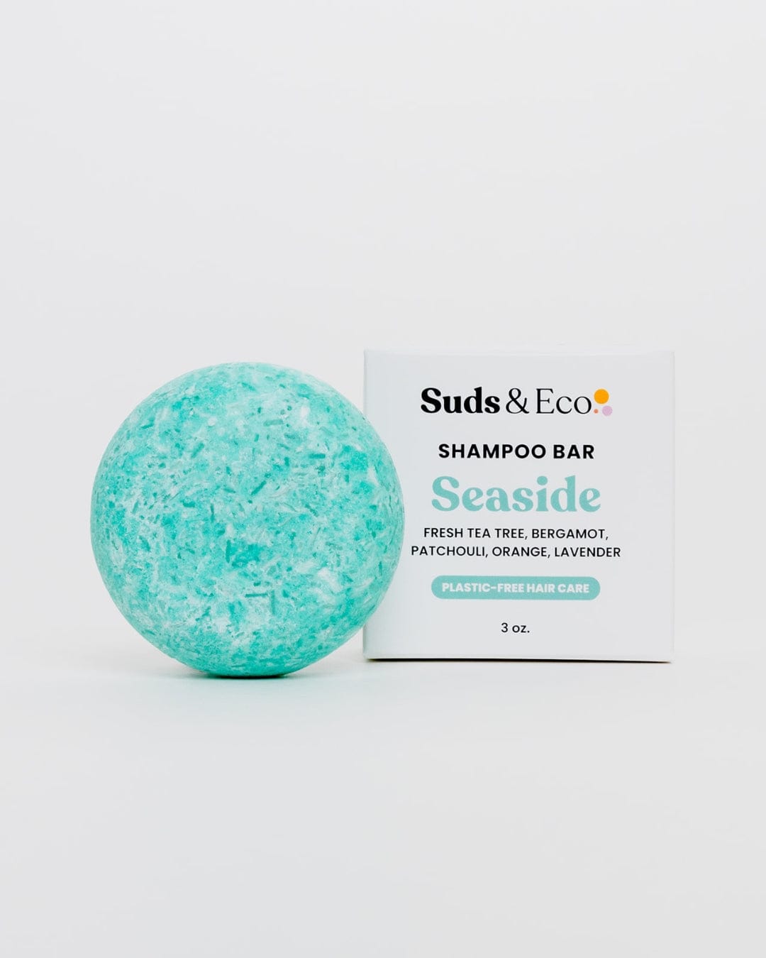 A round turquoise Shampoo Bar from ZeroWasteStore.com sits by a white box labeled "Shampoo Bar Seaside," showcasing zero waste, plastic-free hair care with listed ingredients below.