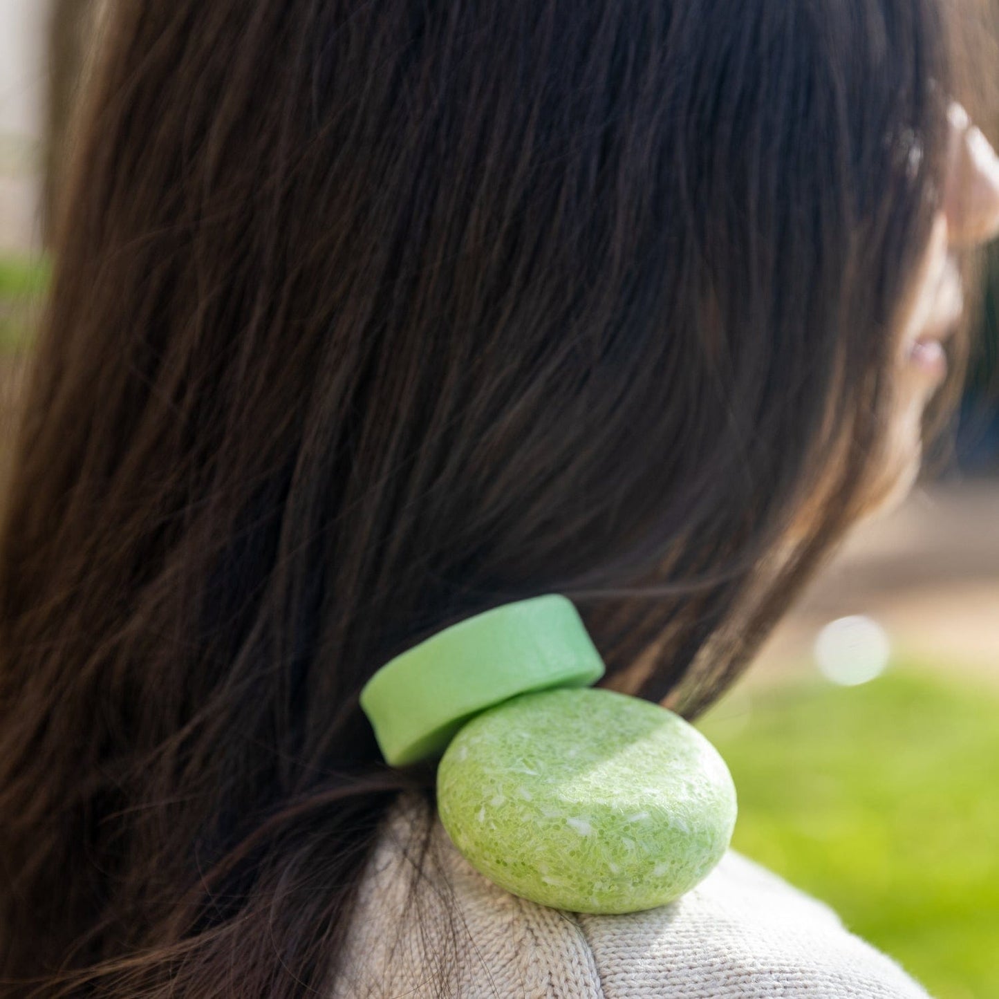 A person with long dark hair balances the ZeroWasteStore.com Shampoo & Conditioner Bar Duo on their shoulder, set against a softly blurred outdoor background.