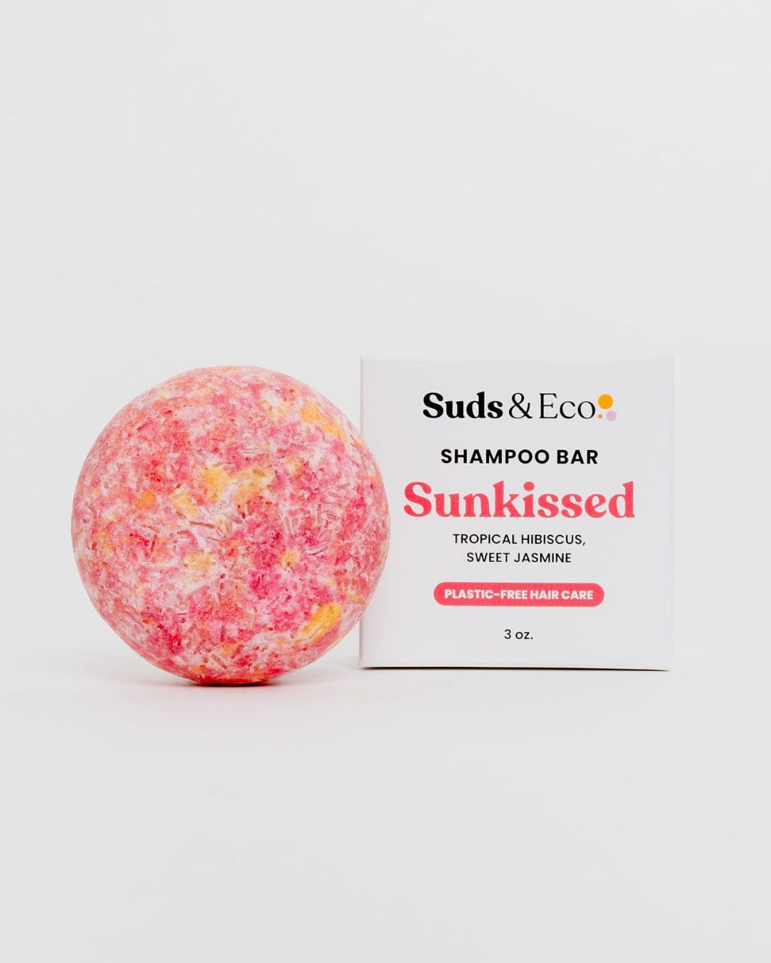 A round, pink and yellow vegan Shampoo Bar by ZeroWasteStore.com sits next to its box labeled "Shampoo Bar, Plastic-Free Hair Care, 3 oz." on a white background—an SLS-free option for zero waste hair care.
