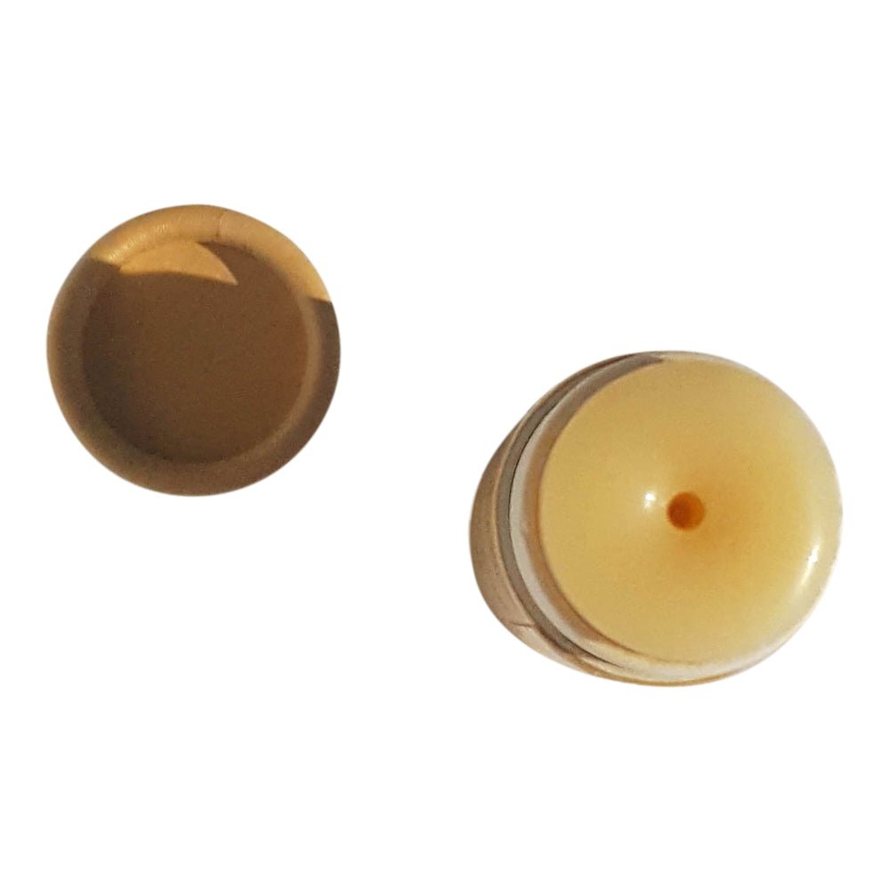 A small, beige plastic cap with a rounded top is shown with a matching beige lid beside it. The cap, belonging to the River Organics Bare Vegan Lip Balm, has a central hole, and both pieces are isolated against a white background.