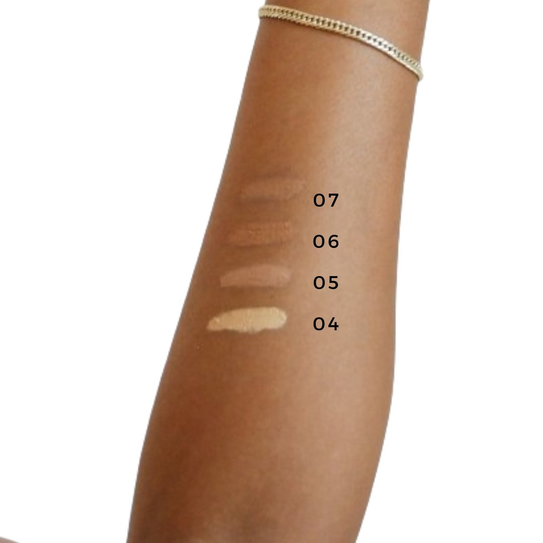 A forearm displaying swatches of four different shades of Zero-Waste Concealer by River Organics, labeled from top to bottom as 07, 06, 05, and 04. The skin tone transitions from light to dark with each shade. Highlighting a plant-based formula and Certified Organic oils, the person is wearing a thin chain bracelet on their wrist.