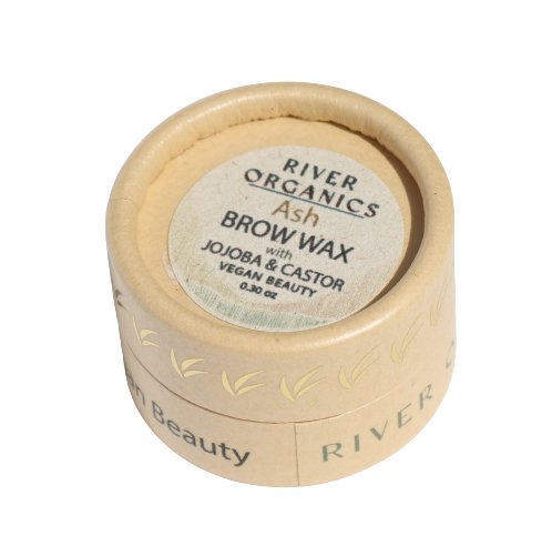 A small round container of **River Organics Tinted Vegan Eyebrow Wax | Ash**, with jojoba and castor. The beige cardboard packaging features green text and decorative leaf designs, indicating that it is a vegan certified beauty product containing 0.32 oz (9 g) of tinted brow wax inside. Eco-friendly and effective!