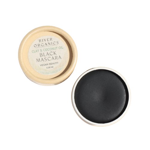 An open container of River Organics Black Zero-Waste Mascara made with clay and coconut oil. The small, round, beige pot features a label that reads "River Organics, Clay & Coconut Oil, Black Zero-Waste Mascara, Vegan Beauty, 0.32 oz." With the lid placed beside the pot, this chemical-free mascara is an eco-friendly beauty choice.