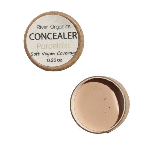 An open container of River Organics Sample Size | Zero Waste Concealer, labeled "Porcelain" and "Soft Vegan Coverage" with a net weight of 0.25 oz. The container reveals a beige-colored cream concealer enriched with organic plant oils, offering buildable coverage for flawless skin.